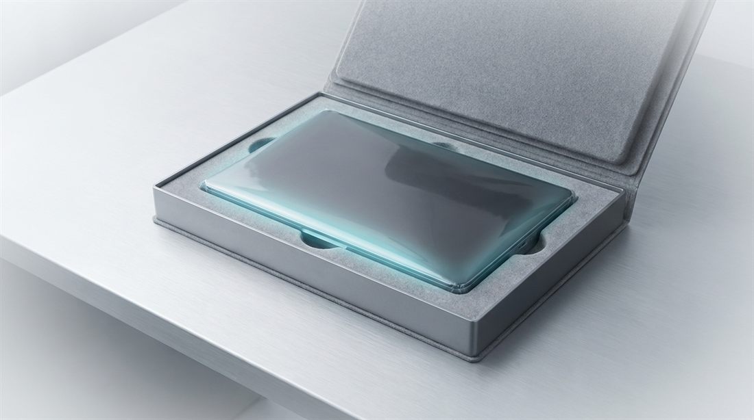 A sleek device glowing faintly, still sealed in its shipping box on an aluminum table — bought, never deployed